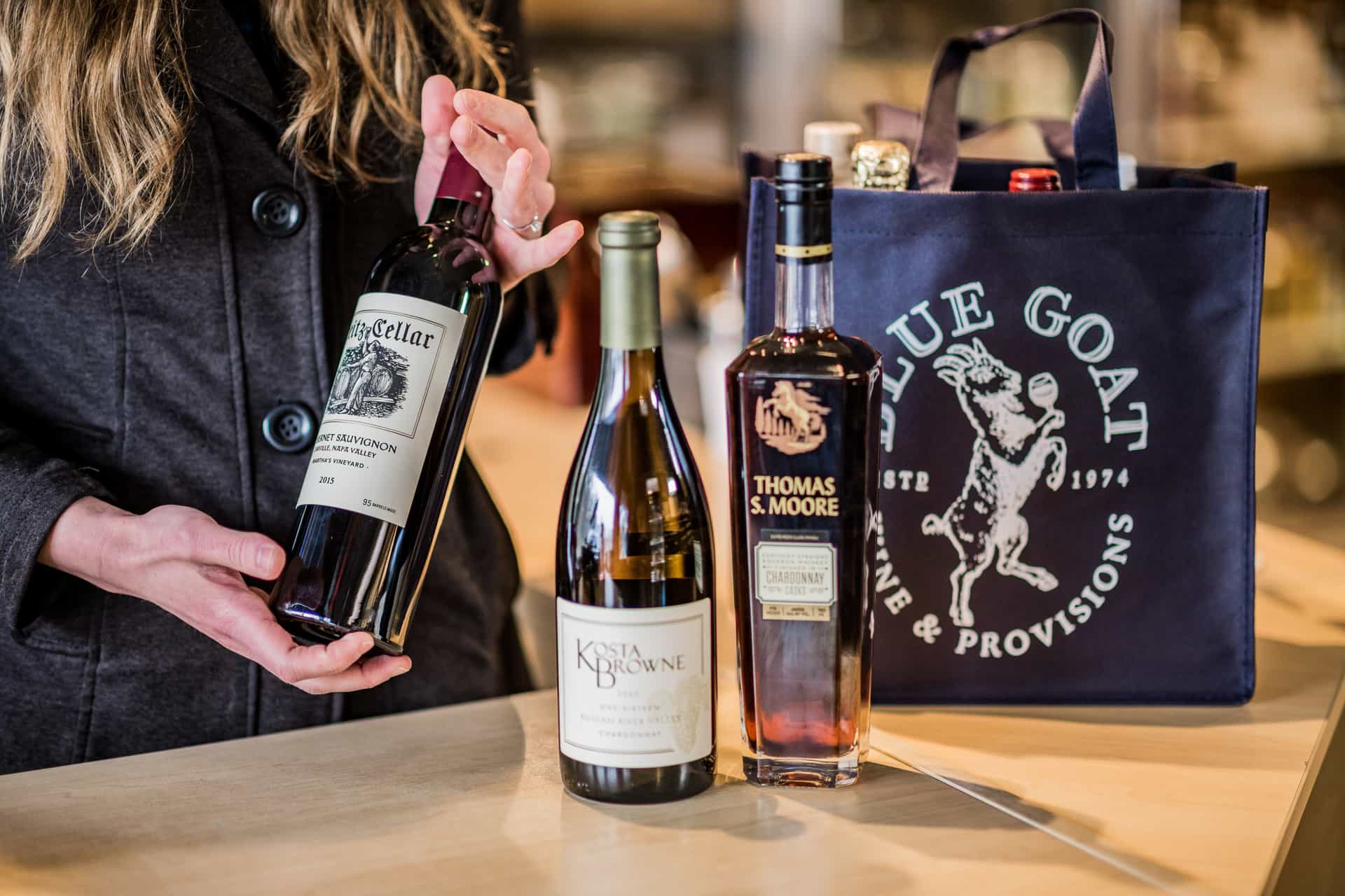 An employee preparing to pack a Blue Goat tote with bottles of wine and spirits.