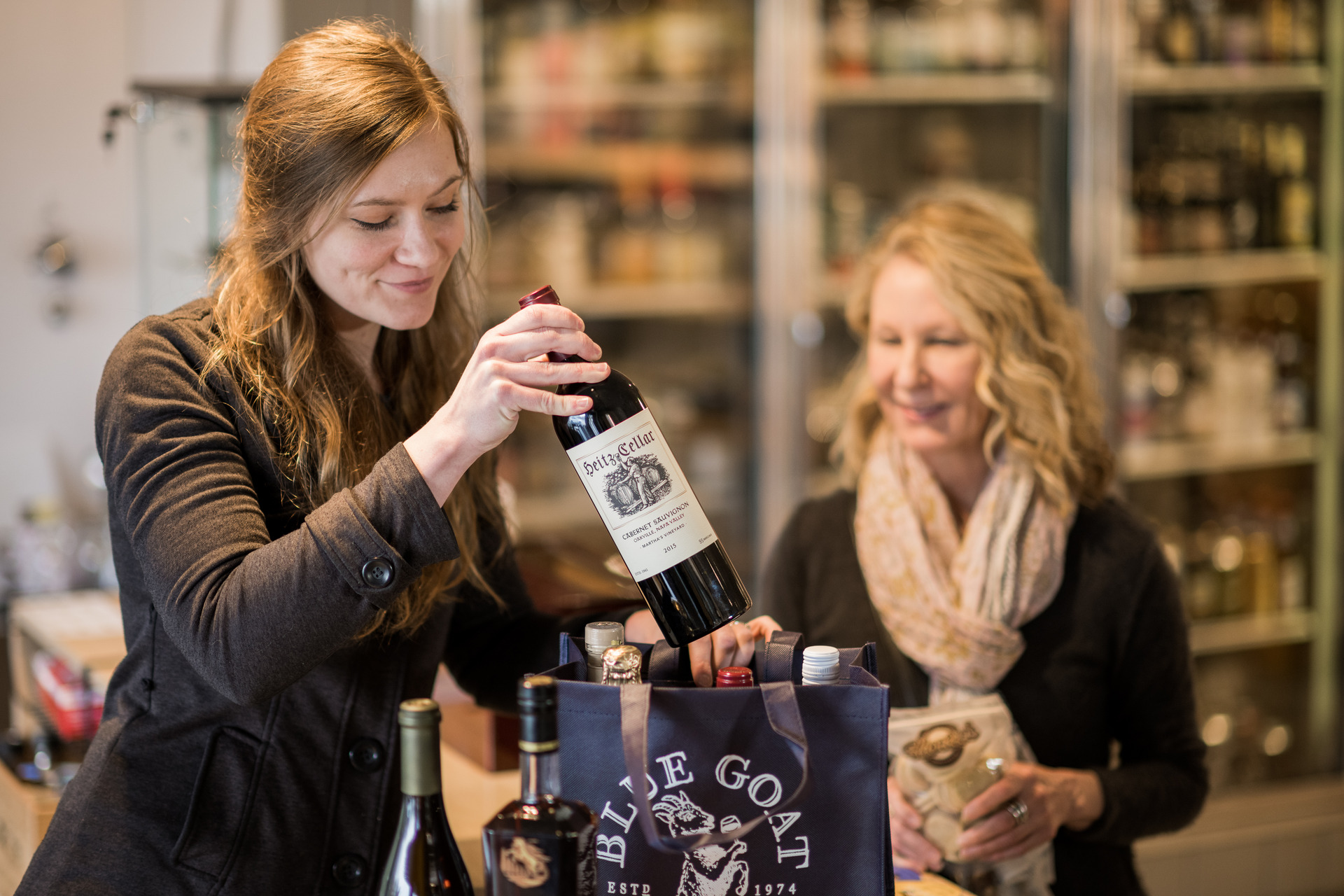 An employee packing a Blue Goat tote with bottles for a waiting customer.